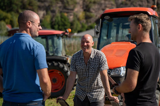 Three men talking and laughing in front of tractors