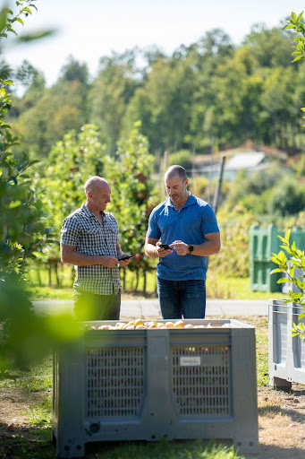Two men talking while looking at their phones on a farm.